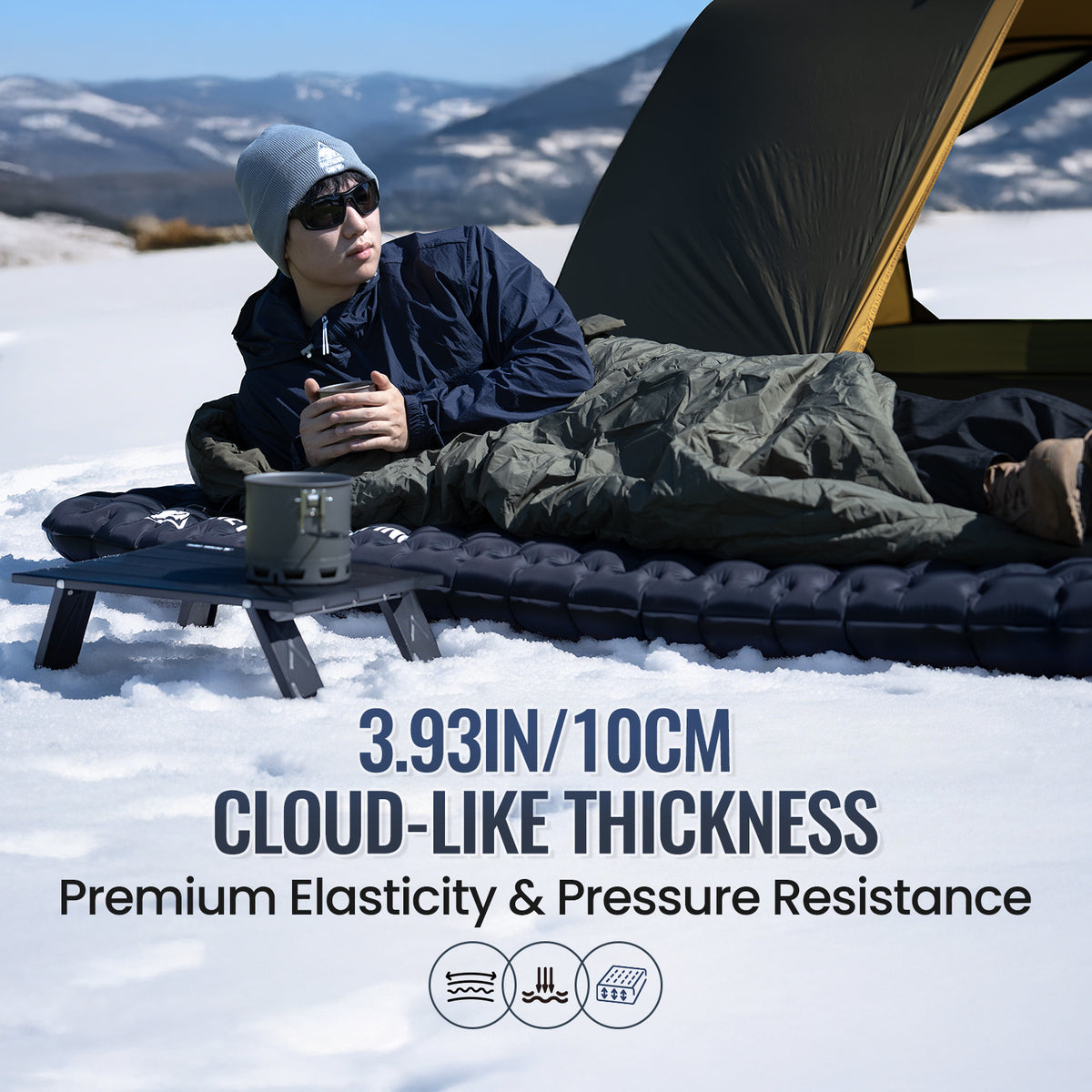 Person lying on a cloud-like thickness camping mattress in the snow with mountains in the background.