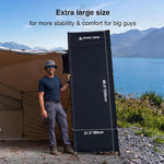 Person holding a large camping cot next to a tent with mountains and lake in the background