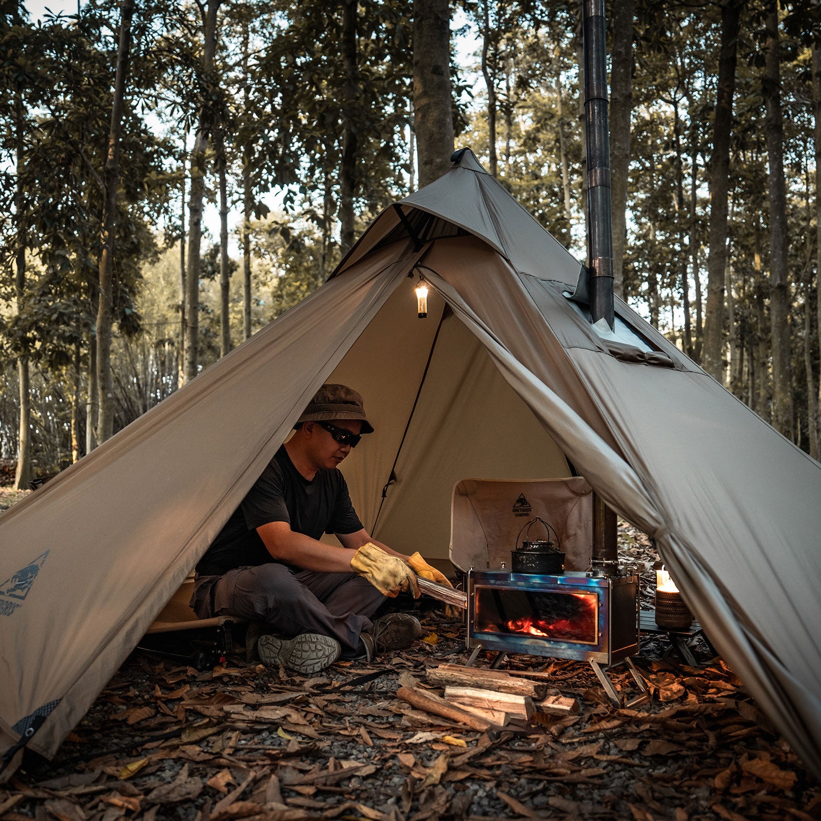 Person camping in a tent using a wood stove in a forest setting