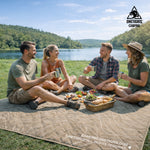 Group of people enjoying a picnic on a blanket by a lake with OneTigris Camping branding.