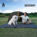 Person with a dog on an OASISMAT camping mat in a grassy field with a tent in the background.