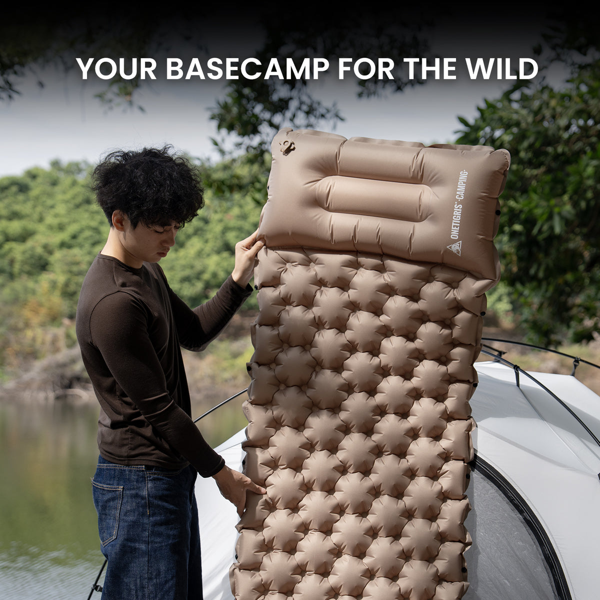 Person setting up an inflatable camping mattress outdoors with a scenic background.
