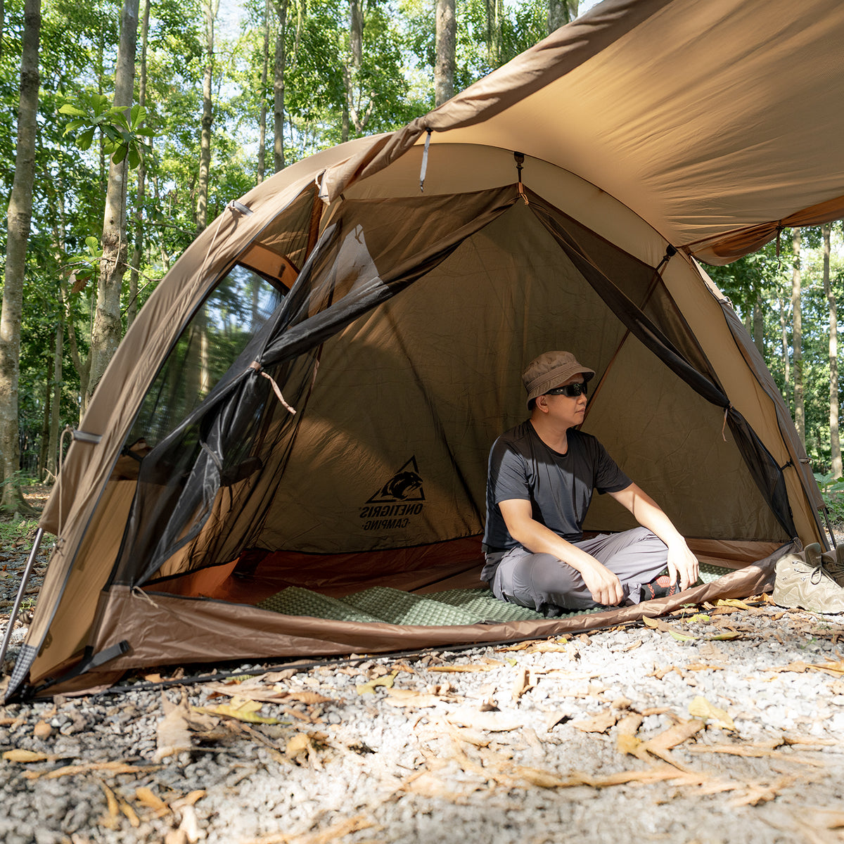 Person sitting inside a brown tent in a forest setting