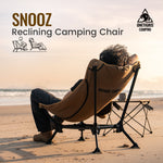 Person using a reclining camping chair on a beach with 'SNOOZ' and 'ONEGRIS CAMPING' branding.