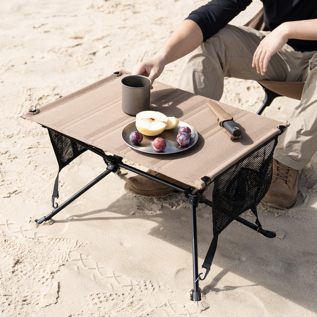 Portable camping table with food on a sandy surface