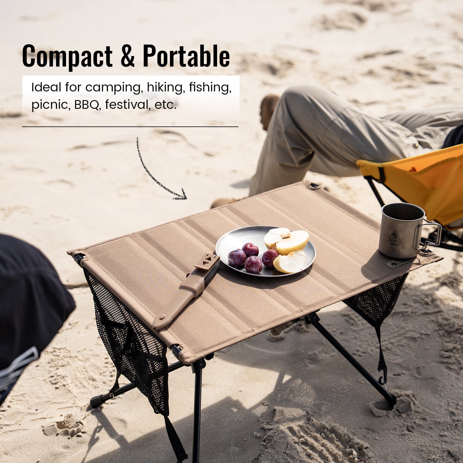 Compact portable table on a sandy surface with food and a cup, ideal for outdoor activities.